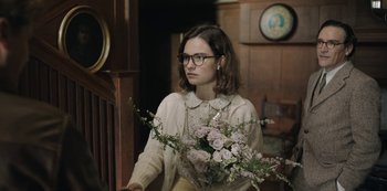Movie still from “The Dig” (2021), directed by Simon Stone – A woman holding a bouquet of flowers in a room; Medium shot, Over the shoulder angle