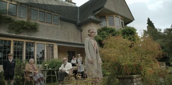 Movie still from “The Dig” (2021), directed by Simon Stone – A woman standing in front of a group of people in front of a house; Wide shot, Low angle