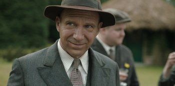Movie still from “The Dig” (2021), directed by Simon Stone – An older man wearing a hat and a suit; Close Up shot, Over the shoulder angle