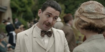 Movie still from “The Dig” (2021), directed by Simon Stone – A man in a suit and bow tie looking to his left; Close Up shot, Over the shoulder angle