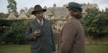 Movie still from “The Dig” (2021), directed by Simon Stone – An older man in a suit talking to an older woman in a hat; Medium shot, Over the shoulder angle
