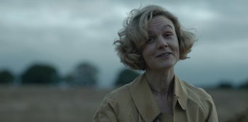 Movie still from “The Dig” (2021), directed by Simon Stone – A woman in a tan jacket is looking at the camera; Close Up shot, Over the shoulder angle