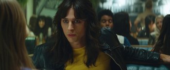 Movie still from “The Dirt” (2019), directed by Jeff Tremaine – A person with long hair wearing a yellow shirt and a black jacket; Close Up shot, Over the shoulder angle