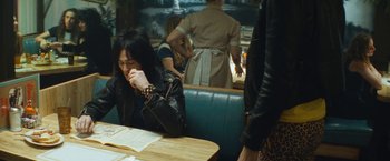 Movie still from “The Dirt” (2019), directed by Jeff Tremaine – A woman sitting at a booth in a restaurant; Medium shot, High angle
