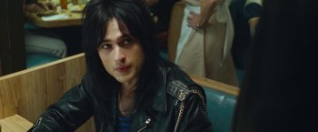 Movie still from “The Dirt” (2019), directed by Jeff Tremaine – A man with long black hair sitting in a chair; Close Up shot, Over the shoulder angle