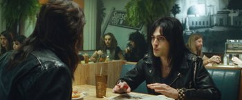 Movie still from “The Dirt” (2019), directed by Jeff Tremaine – A man sitting at a table in front of two other people; Medium shot, Over the shoulder angle