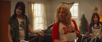 Movie still from “The Dirt” (2019), directed by Jeff Tremaine – A woman holding a beer while holding a guitar in a room; Medium shot, Over the shoulder angle