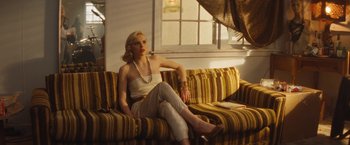 Movie still from “The Dirt” (2019), directed by Jeff Tremaine – A woman sitting on top of a couch in a living room; Medium shot, Over the shoulder angle