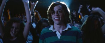 Movie still from “The Dirt” (2019), directed by Jeff Tremaine – A man with long hair is smiling in a crowd; Medium shot, Low angle