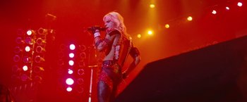 Movie still from “The Dirt” (2019), directed by Jeff Tremaine – A woman in a red outfit singing on a stage; Wide shot, Low angle