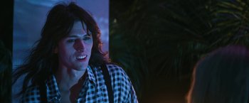 Movie still from “The Dirt” (2019), directed by Jeff Tremaine – A man with long hair and a checkered shirt is smiling; Close Up shot, Low angle