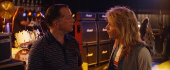 Movie still from “The Dirt” (2019), directed by Jeff Tremaine – A man and a woman talking to each other in front of a wall of amps; Close Up shot, Over the shoulder angle