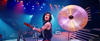 Movie still from “The Dirt” (2019), directed by Jeff Tremaine – A man in a black shirt is playing a musical instrument; Wide shot, High angle