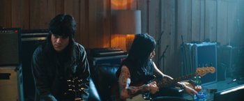 Movie still from “The Dirt” (2019), directed by Jeff Tremaine – A man and a woman sitting on a couch with guitars; Medium shot, Over the shoulder angle
