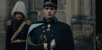 Movie still from “The Empress” (2022), created by Katharina Eyssen – A man in a military uniform stands in front of a stone wall; Medium shot, Over the shoulder angle