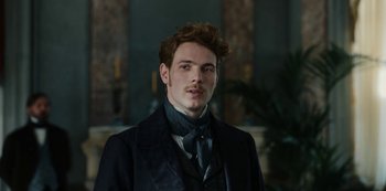 Movie still from “The Empress” (2022), created by Katharina Eyssen – A man in a suit and tie standing in front of a fireplace; Close Up shot, Low angle