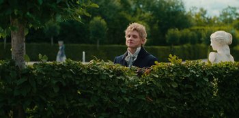 Movie still from “The Empress” (2022), created by Katharina Eyssen – A man standing behind a hedge in a park; Medium shot, Over the shoulder angle