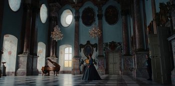 Movie still from “The Empress” (2022), created by Katharina Eyssen – A woman in a blue dress sitting in front of a grand piano; Extreme Wide shot, Low angle