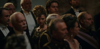 Movie still from “The Empress” (2022), created by Katharina Eyssen – A group of people standing in a room; Close Up shot, Over the shoulder angle
