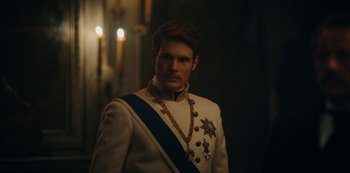 Movie still from “The Empress” (2022), created by Katharina Eyssen – A man in a white and blue suit standing in front of candles; Close Up shot, Over the shoulder angle