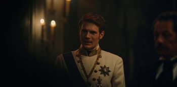 Movie still from “The Empress” (2022), created by Katharina Eyssen – A man in a white suit with a gold chain around his neck; Close Up shot, Over the shoulder angle