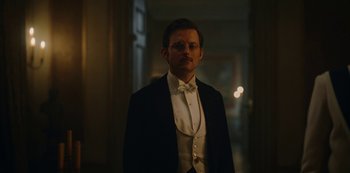 Movie still from “The Empress” (2022), created by Katharina Eyssen – A man in a tuxedo standing in a room; Medium shot, Low angle