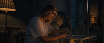 Movie still from “No Time to Die” (2021), directed by Cary Joji Fukunaga – A woman writing on a piece of paper in front of a mirror; Medium shot, High angle
