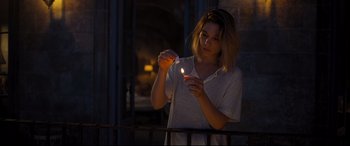 Movie still from “No Time to Die” (2021), directed by Cary Joji Fukunaga – A woman lighting a candle on a balcony railing at night; Medium shot, Over the shoulder angle