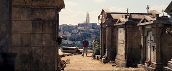 Movie still from “No Time to Die” (2021), directed by Cary Joji Fukunaga – A man walking through a cemetery with a view of a city in the background; Extreme Wide shot, High angle