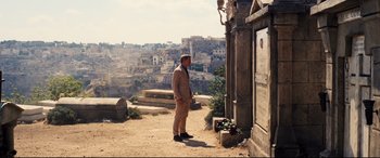 Movie still from “No Time to Die” (2021), directed by Cary Joji Fukunaga – A man standing in front of a building in the middle of the desert; Wide shot, Over the shoulder angle