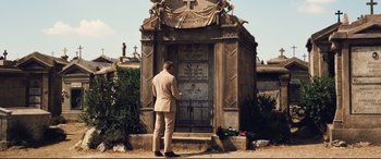Movie still from “No Time to Die” (2021), directed by Cary Joji Fukunaga – A man standing in front of an old grave; Wide shot, Over the shoulder angle