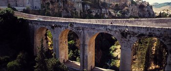 Movie still from “No Time to Die” (2021), directed by Cary Joji Fukunaga – A person is jumping off a bridge over a river; Extreme Wide shot, Overhead angle