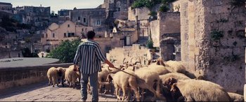 Movie still from “No Time to Die” (2021), directed by Cary Joji Fukunaga – A man herding a herd of sheep down a street; Wide shot, High angle