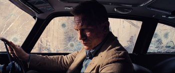 Movie still from “No Time to Die” (2021), directed by Cary Joji Fukunaga – A man in a suit driving in a car with bullet holes in the windshield; Medium shot, Over the shoulder angle