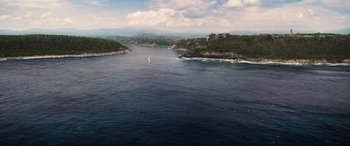 Movie still from “No Time to Die” (2021), directed by Cary Joji Fukunaga – A view of a body of water with a sailboat in it; Extreme Wide shot, High angle