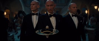 Movie still from “No Time to Die” (2021), directed by Cary Joji Fukunaga – A man in a tuxedo holding a tray with a ring on it; Medium shot, Low angle