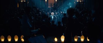 Movie still from “No Time to Die” (2021), directed by Cary Joji Fukunaga – A crowd of people standing in a dark room; Wide shot, Over the shoulder angle