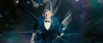 Movie still from “No Time to Die” (2021), directed by Cary Joji Fukunaga – A man in a suit and bow tie standing on a staircase; Wide shot, Overhead angle