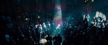 Movie still from “No Time to Die” (2021), directed by Cary Joji Fukunaga – A group of people in suits and ties standing in front of a crowd; Wide shot, High angle