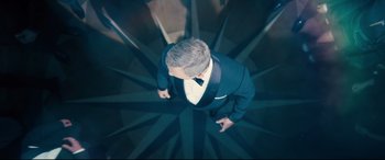 Movie still from “No Time to Die” (2021), directed by Cary Joji Fukunaga – A man wearing a suit and bow tie standing on a spiral staircase; Wide shot, Overhead angle