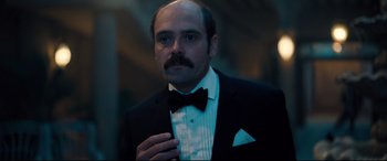 Movie still from “No Time to Die” (2021), directed by Cary Joji Fukunaga – A man in a suit and bow tie; Close Up shot, Over the shoulder angle