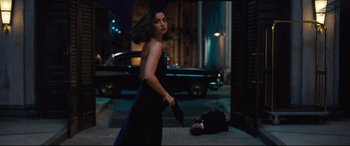 Movie still from “No Time to Die” (2021), directed by Cary Joji Fukunaga – A woman in a black dress holding a gun and a man laying on the ground; Wide shot, Over the shoulder angle