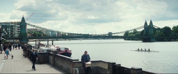 Movie still from “No Time to Die” (2021), directed by Cary Joji Fukunaga – A man sitting on the edge of a pier next to a body of water; Extreme Wide shot, High angle