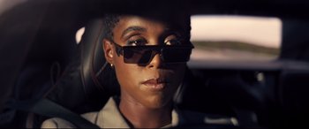 Movie still from “No Time to Die” (2021), directed by Cary Joji Fukunaga – A woman wearing sunglasses sitting in a car; Close Up shot, Over the shoulder angle