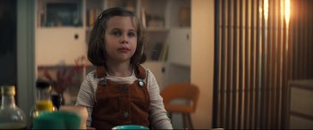 Movie still from “No Time to Die” (2021), directed by Cary Joji Fukunaga – A little girl sitting at a table in front of a bookshelf; Close Up shot, High angle