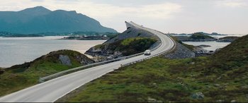 Movie still from “No Time to Die” (2021), directed by Cary Joji Fukunaga – A car driving down a road next to a body of water; Extreme Wide shot, High angle