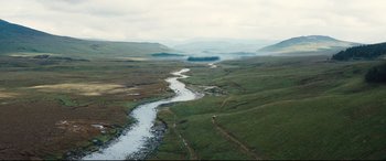 Movie still from “No Time to Die” (2021), directed by Cary Joji Fukunaga – A river running through a lush green field; Extreme Wide shot, High angle