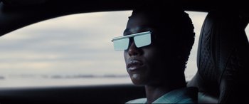 Movie still from “No Time to Die” (2021), directed by Cary Joji Fukunaga – A man wearing a pair of sunglasses in a car; Close Up shot, Low angle