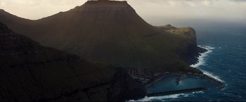 Movie still from “No Time to Die” (2021), directed by Cary Joji Fukunaga – A view of a mountain with a body of water in the foreground; Extreme Wide shot, High angle