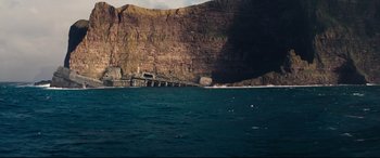 Movie still from “No Time to Die” (2021), directed by Cary Joji Fukunaga – A body of water near a cliff and a bridge; Extreme Wide shot, High angle